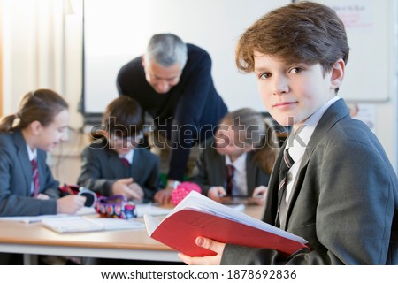 Portrait shot of a middle school student with a notebook standing in a classroom.