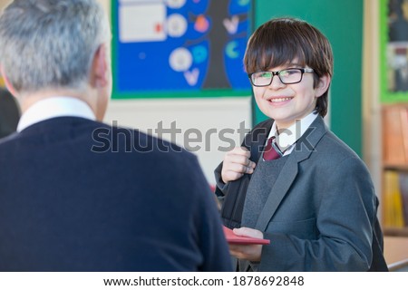 Middle school student in uniform turning in his homework to a teacher in the classroom.