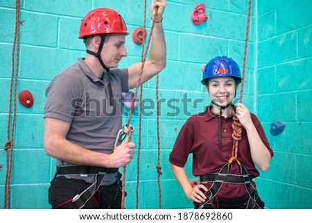 Portrait shot of a high school student in harness standing with a gym teacher against a rock climbing wall.
