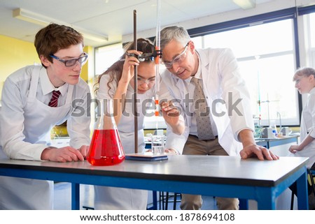Chemistry teacher guiding high school students while they conduct a scientific experiment.
