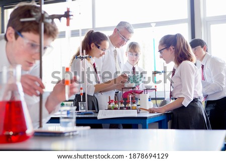 Chemistry teacher guiding high school students while they conduct a scientific experiment using a burner.