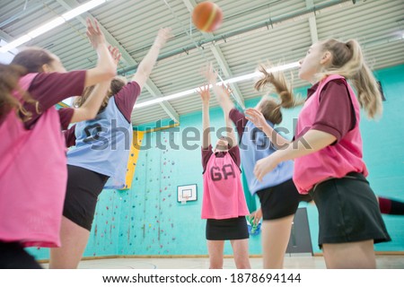 High school girls jumping and playing basketball during a gym class.
