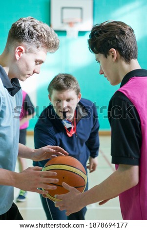Gym teacher initiating a basketball tip-off for high school students.