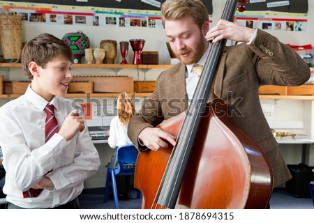 Music teacher playing a double bass in a music class with a middle school student watching him.