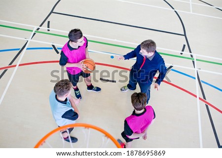 High-angle shot of a gym teacher guiding high school students with a basketball during a gym class.