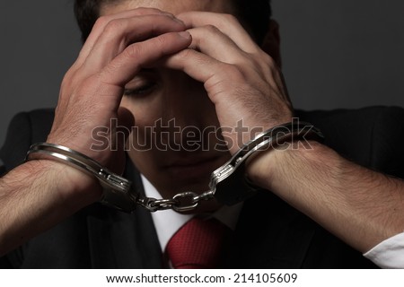 Handcuffed businessman covering his face with his hands.