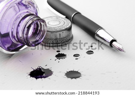Closeup of a pen and inkwell with inkblots on a paper.