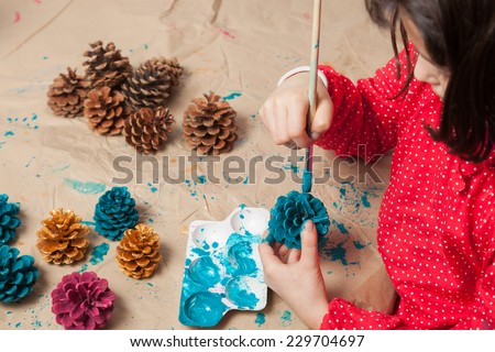 Child painting pine cones as Christmas ornaments.