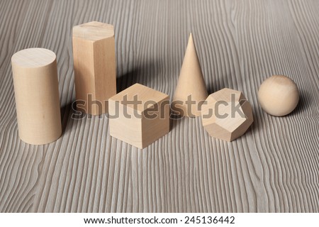 Wood geometric shapes on a wood surface. Cylinder, prism, cube, cone, polyhedron and sphere.