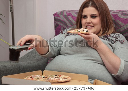 Woman with overweight eating pizza and watching tv on the couch