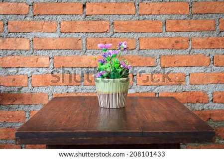 Fake flowers on the table with a brick wall background.
