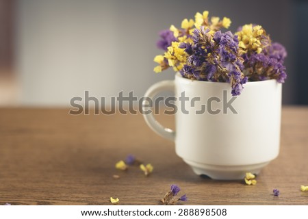 Dried flowers in a white coffee cup and placed on a wooden table.Warm tone photo.