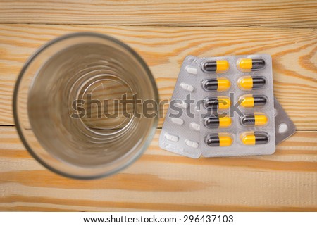 packaging of pills and capsules of medicines and a glass of water placed on a wooden table, warm tone photo.