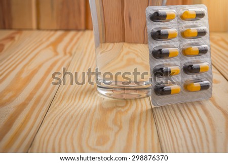 packaging of pills and capsules of medicines and a glass of water placed on a wooden table, warm tone photo.