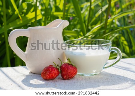Strawberry with leaves, a cup of milk, a pitcher on a napkin on a grass background