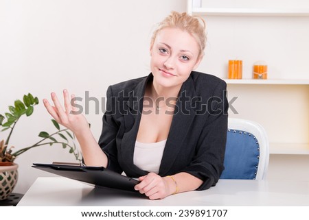 Pretty woman in a jacket gesturing at his desk at work - studio shoot