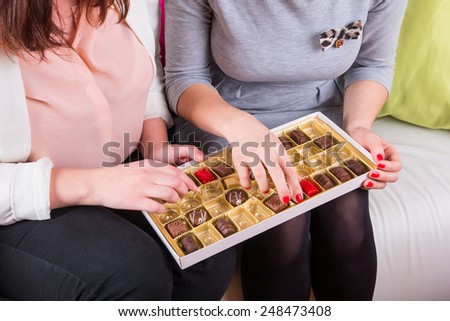 Womens on the couch eating a box of sweet chocolates