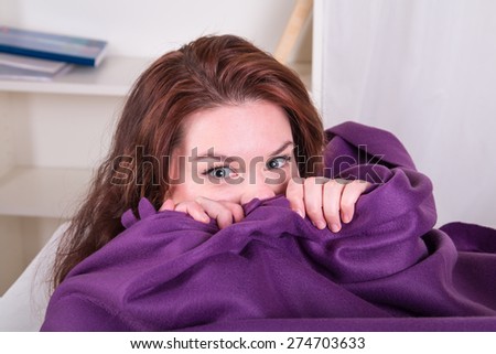 Frightened woman hiding under a blanket - home