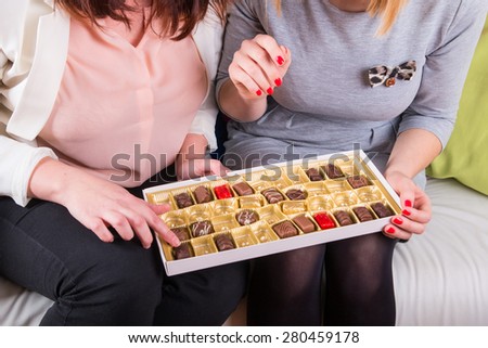 Womens on the couch eating a box of sweet chocolates