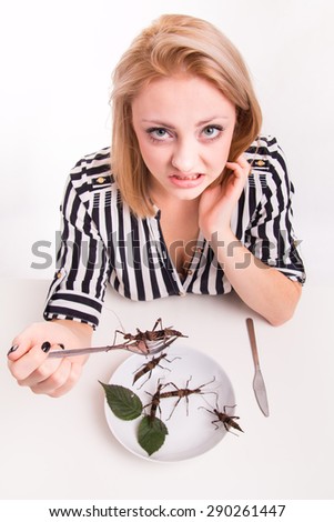 Disgusted woman eating big insects with a fork in a restaurant