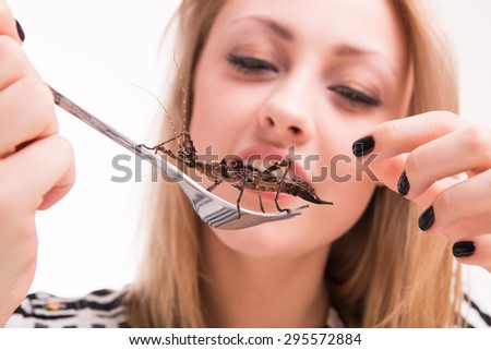 Woman eating big insects with a fork in a restaurant