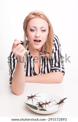Joyful woman eating big insects with a fork in a restaurant