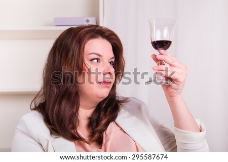Plump and elegant woman tests a glass of red wine