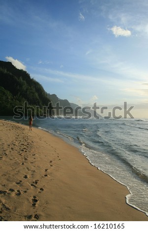 Woman in a red bikini walking down the beach on the north sore of Kauai.
