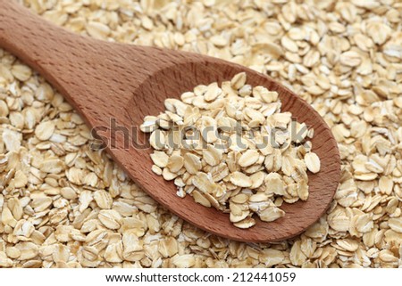 Rolled oats (oat flakes) in a wooden spoon on a rolled oats background. Close-up.