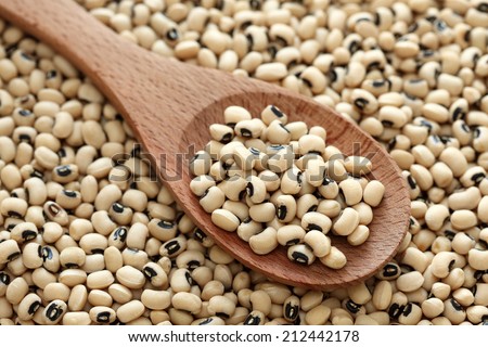 Black eyed peas in a wooden spoon on a black eyed peas background. Close-up.
