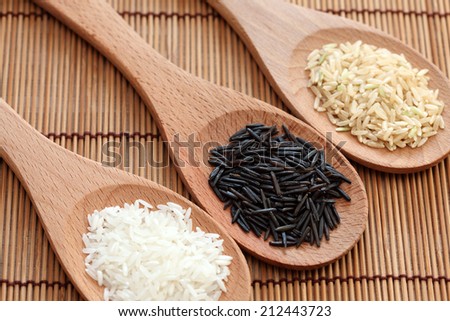 White rice and wild rice in a wooden spoons on bamboo napkin. Focus on a wild rice. Close-up.