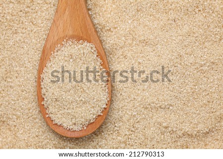 Brown cane sugar in a wooden spoon on brown cane sugar background. Close-up.