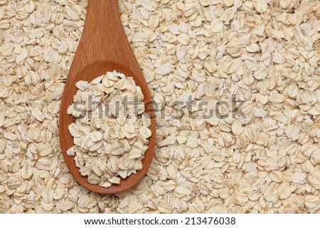 Rolled oats (oat flakes) in a wooden spoon on a rolled oats background. Closeup.
