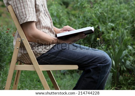 Student reading book sitting on folding chair outdoors.