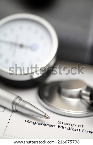 Blood Pressure Gauge (shygmomanometer, stethoscope, cuff) and ballpoint pen on medical records. Focus on ballpoint pen.