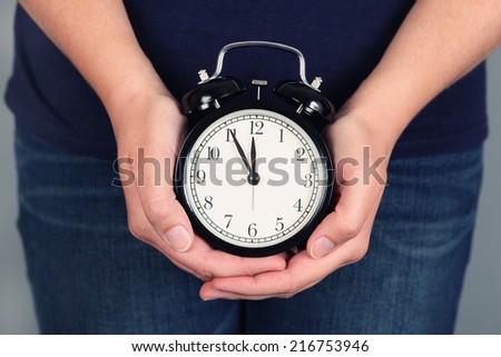 Woman\'s hands holding and showing alarm clock. Five minutes before deadline.