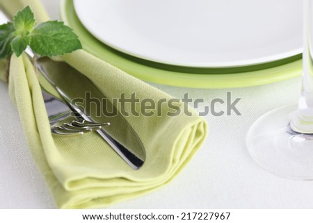 Table setting with fork, knife on green napkin and plate with glass on a tablecloth. (Place setting).