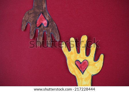 White and Black paper hands hold red paper hearts against red background.