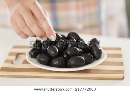 Woman\'s hand takes one black olive from plate with black olives.