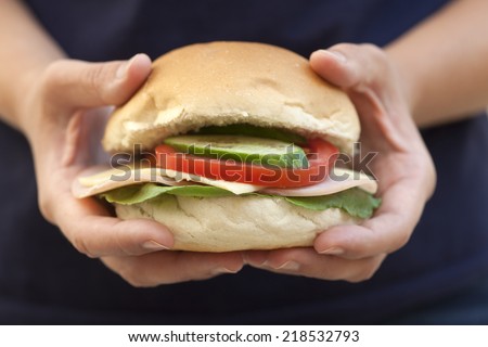 Homemade hamburger in woman's hands. Fresh ingredients only: Tomato, Cucumber, Cheese,  Lettuce, Turkey breast ham, Bun.