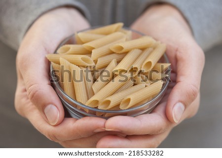 Organic brown rice pasta penne in a bowl in woman\'s hands. (Gluten Free Product).
