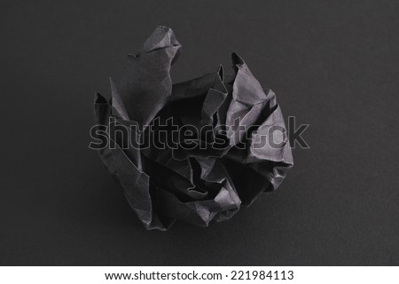 Crumpled black paper ball on a black background.