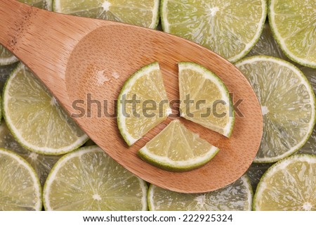 Lime slices in a wooden spoon on lime slices background. Closeup.