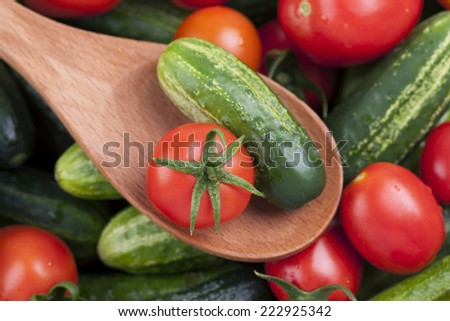 Tomato and cucumber in a wooden spoon on tomatoes and cucumbers background. Closeup.
