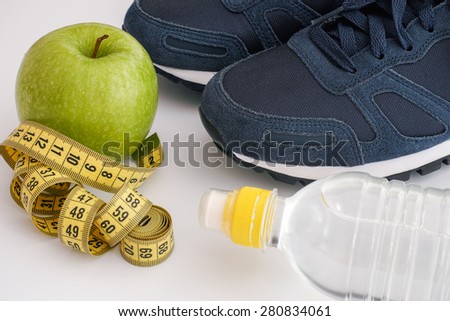 Sport shoes with bottle of water, green apple and tape measure on white background. Closeup.