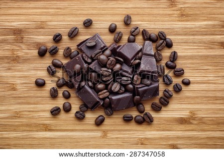 Heap of broken dark organic chocolate and coffee beans on a natural wooden background.