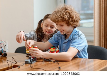 Boy and girl doing a group project, making a robot from a plastic block kit. Happy emotion and enjoyment.