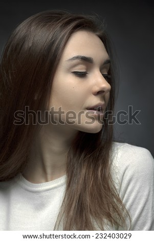 Young woman posing in a white sweater with closed eyes on a black background.Without makeup.