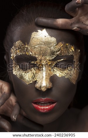 Beauty portrait of a brown-skinned girl with golden makeup of foil closed eyes and red lips.