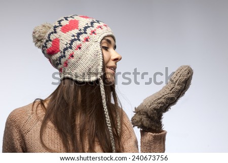Beautiful young woman in a warm hat and in light brown mittens on a gray background.